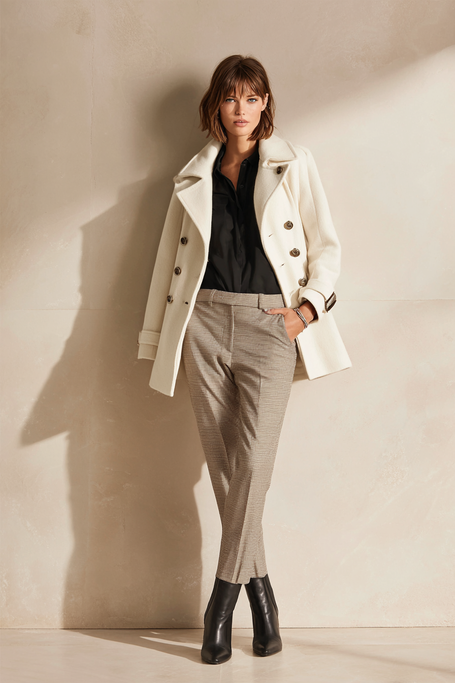An elegant outfit featuring a tailored ivory blazer over a flowy cream silk blouse, paired with dark olive wide-leg trousers and polished beige heels. A delicate gold pendant necklace and a chic structured handbag complete the ensemble. The model stands in soft studio lighting against a clean bokeh backdrop, exuding timeless luxury.
