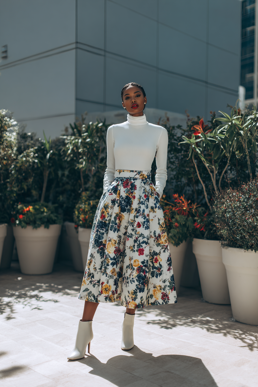 A model showcasing a tailored white linen jumpsuit with wide legs, complemented by sleek beige block-heel sandals and a chic woven clutch, standing against a minimal cream wall, elegantly posed with a glass of sparkling drink --ar 2:3 --v 7 --style raw