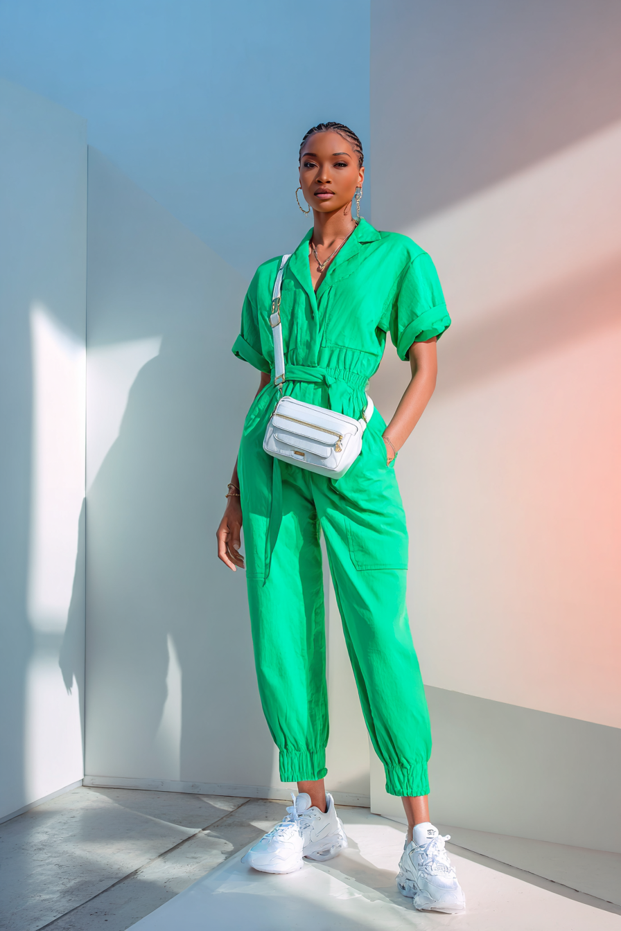 A vibrant outfit featuring a tailored jumpsuit in a vivid color paired with casual white sneakers for an unexpected twist. The model carries a chic crossbody bag, set in a bright, airy space with soft studio lighting, creating a look that is both playful and sophisticated --ar 2:3 --v 7 --style raw